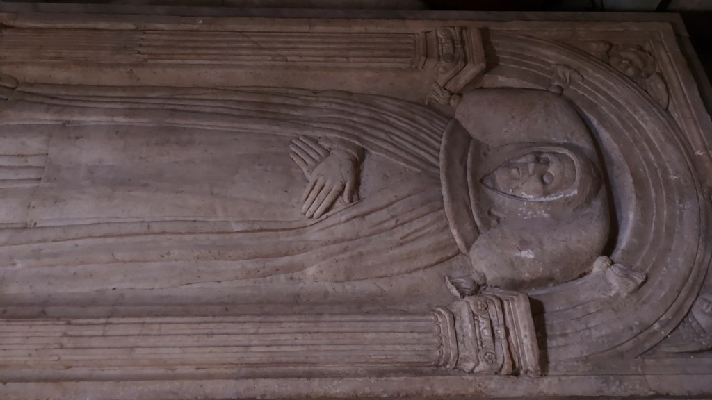 Marmoriin veistetty hautapaikka, joka esittää lepäävää ihmistä, jolla on kädet vatsan päällä.